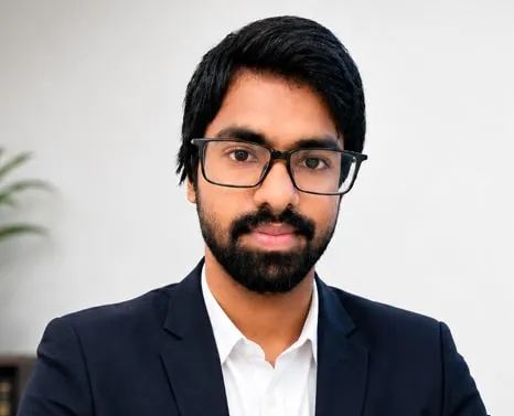 CA Kiran Teja, Partner at SRI TEJ & ASSOCIATES, wearing glasses and a navy blazer in an office setting.